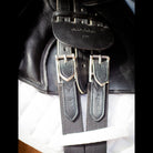 Close-up of the black EcoRider girth buckled to the saddle billets, showing the size 52 stamp and debossed branding.
